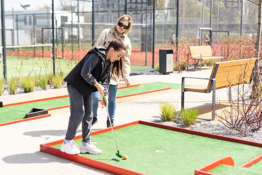 Mother playing with her cute daughter in mini golf.