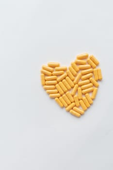 Yellow pills in the shape of a heart, health and heart problems. The concept of medicine and healthcare. Place for an inscription, vertical photo