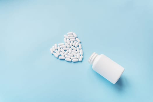 White pills in the shape of a heart came out of a jar on a blue background, health and heart problems together with a plastic jar. The concept of medicine and health care