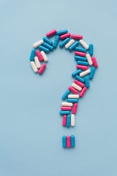 Question mark consisting of three multi-colored vitamins on a blue background. Health problems and treatment. The concept of evidence-based medicine