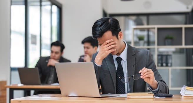 Focused serious professional using laptop in office lobby. Young asian man using laptop in background. Wireless technology concept..