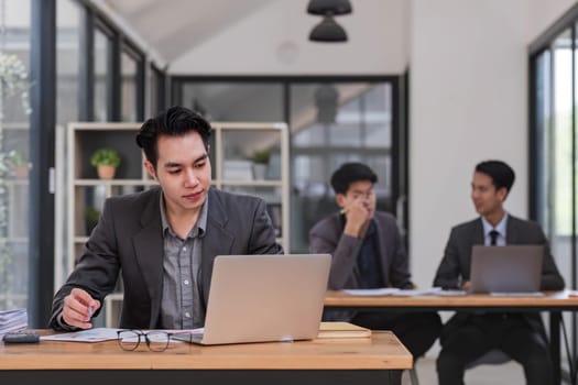 Portrait of confident young businessman using laptop while colleague in background..