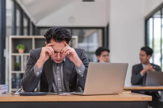 Focused serious professional using laptop in office lobby. Young asian man using laptop in background. Wireless technology concept..