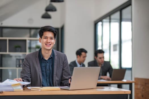 Portrait of confident young businessman using laptop while colleague in background..