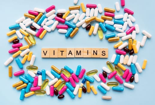 Different colorful pills from different symptoms in the middle - the inscription from wooden letters vitamins. Health and medicine concept