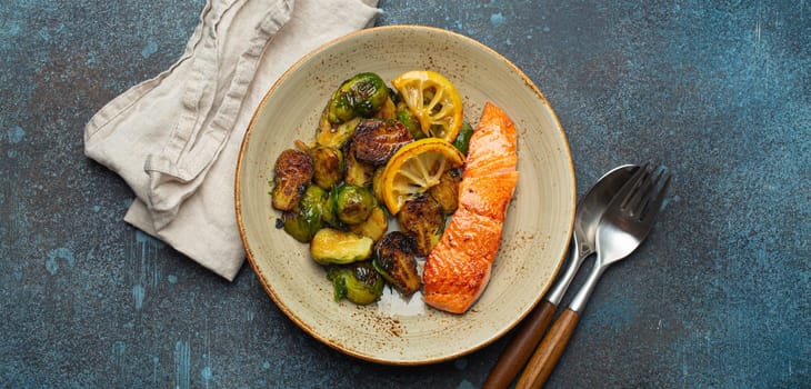 Delicious salmon fillet with grilled Brussels sprouts on plate, rustic stone background top view. Healthy dinner with grilled fish and vegetables, balanced nutrition