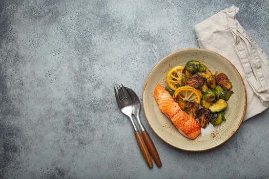 Delicious salmon fillet with grilled Brussels sprouts on plate, rustic stone background top view. Healthy dinner with grilled fish and vegetables, balanced nutrition, space for text