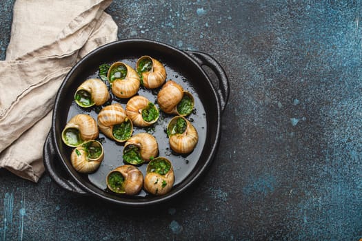 Escargots de Bourgogne Snails with Garlic Butter and Parsley in black cast iron pan on rustic stone background top view, traditional French Delicacy, space for text.