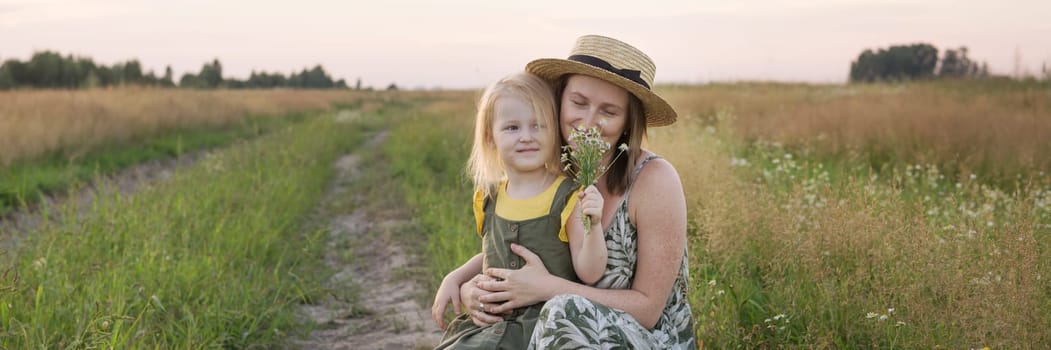 Mom and daughter walk through a chamomile field, and collect a bouquet of flowers. The concept of family relations, nature walks, freedom and a healthy lifestyle