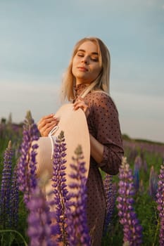 A beautiful woman in a straw hat walks in a field with purple flowers. A walk in nature in the lupin field.