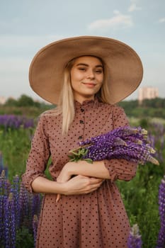 A beautiful woman in a straw hat walks in a field with purple flowers. A walk in nature in the lupin field.