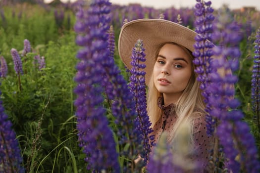 A beautiful woman in a straw hat walks in a field with purple flowers. A walk in nature in the lupin field.