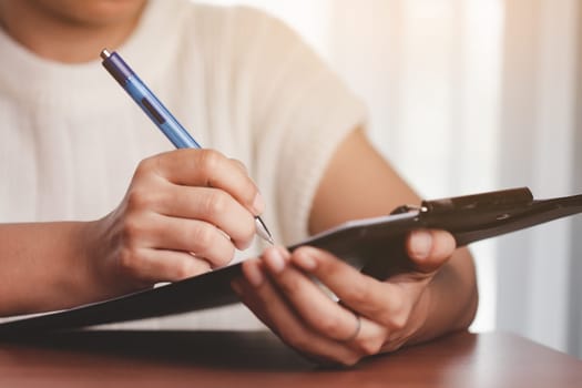 Asian woman's hand holding a pen and writing something on the notebook for the concept of work and study.