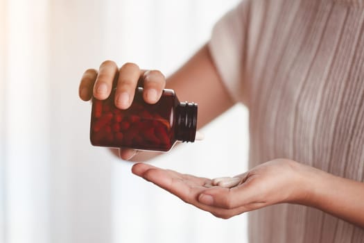 Asian woman's hand pouring medicines from a brown bottle for healthcare concept.