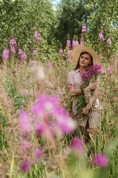 A young woman in nature with a bouquet of pink wild flowers. A bouquet of Ivan-tea in the hands of a woman.