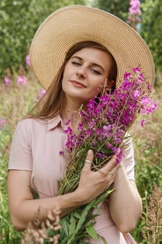 A young woman in nature with a bouquet of pink wild flowers. A bouquet of Ivan-tea in the hands of a woman.