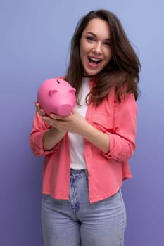 cute brunette young woman in a shirt and jeans saves money for business in a piggy bank.