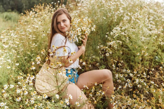 Beautiful young woman in nature with a bouquet of daisies. Field daisies, field of flowers. Summer tender photo.