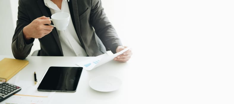 Portrait of a young Asian man showing a smiling face as she uses his phone, computer and financial documents on her desk in the early morning hours.