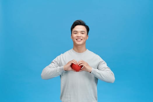 Young man holding red heart over blue background