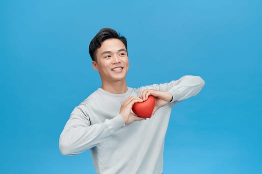 Young man holding red heart over blue background