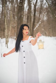 Attractive woman in evening dress standing in the winter forest with hand lamp