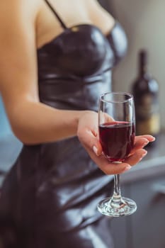 slim woman in a leather dress holds a wineglass with red wine .