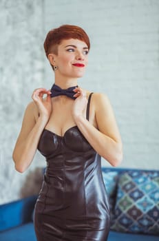 slim woman in a leather dress straightens a butterfly around her neck.