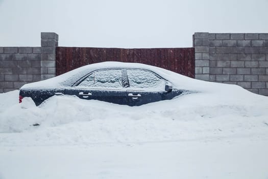 car parked near the fence is completely covered with snow.