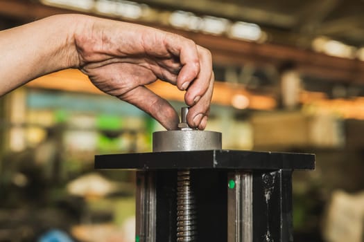 worker tightens a nut on a machine with a dirty hand.