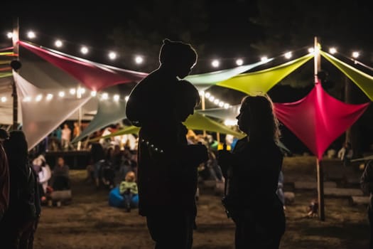 Glebovka, Ukraine, August 2020: Silhouettes of parents with a child at night at the festival