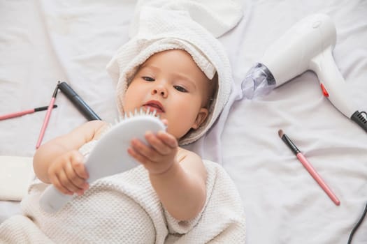 beautiful baby with towel on her head lies near the hairdryer and cosmetics