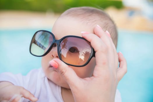 mom put sunglasses on the baby in which palm trees are reflected.