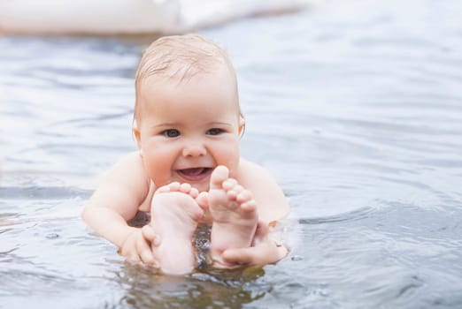 beautiful baby bathes in the water and holds his legs.