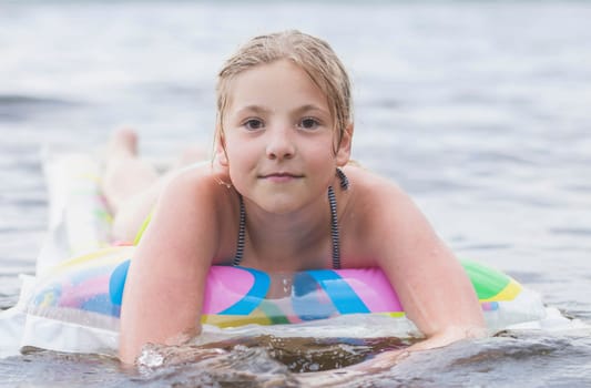 beautiful teenager floating on multi-colored air mattress on the river.