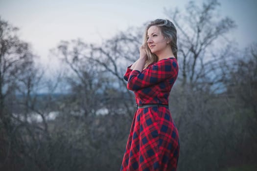 Attractive blonde girl in a red dress in the evening forest.