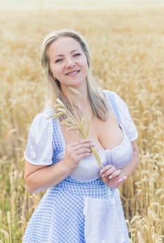 beautiful blonde with big breasts holds spikelets in a field with wheat