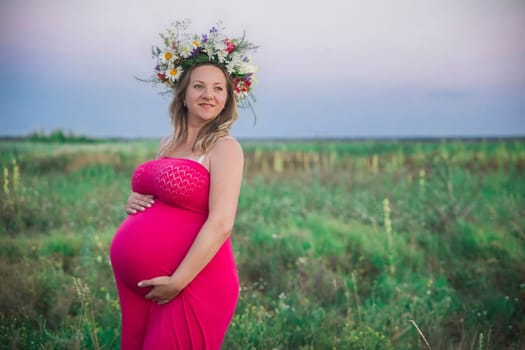 charming pregnant woman with a wreath in the field.