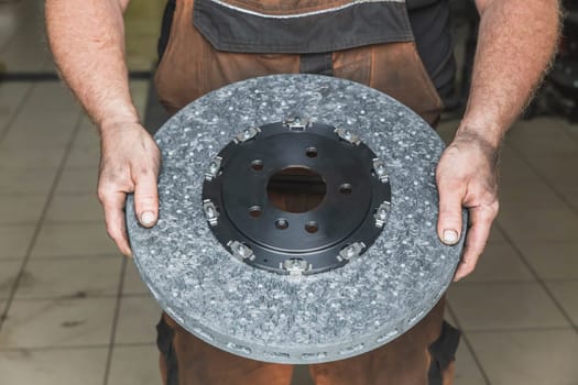 mechanic in a dirty clothes holds a carbon brake disc.