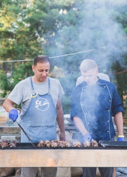 Glebovka, Ukraine, August 2020: two cooks in sterile gloves are grilling meat