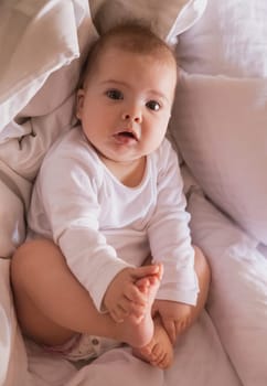 cute baby is lying in bed holding his legs.