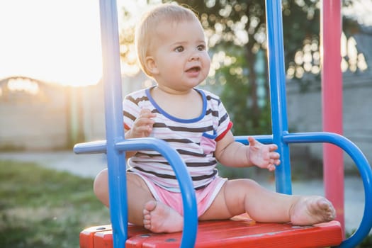 Blonde baby sitting on a swing at sunset.