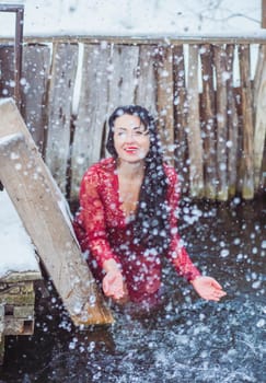 Attractive woman in red dress bathes in the ice-hole in winter.