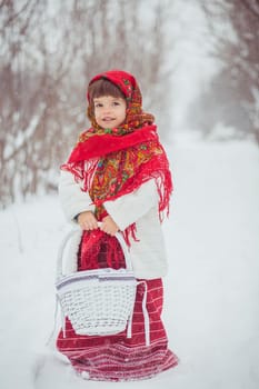 Beautiful little girl in old Ukrainian clothes in a winter forest with wicker basket