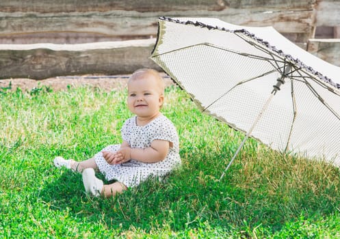 beautiful baby in a polka-dot dress is sitting nea umbrella umbrella.