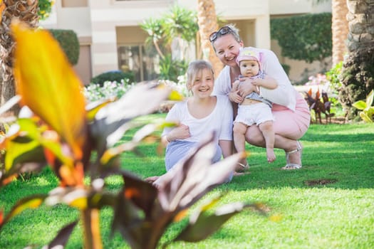 Mom with two daughters sitting on the lawn in the yard.