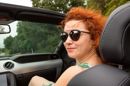 Portrait of beautiful young woman in sunglasses sitting in luxury modern cabriolet car. Portrait happy woman in convertible. travel, road trip and people concept - happy young woman in convertible car