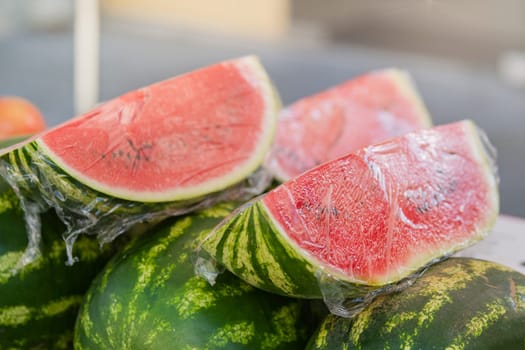 Watermelons in the market. Fresh watermelons are stacked on the counter, cut into pieces and wrapped in plastic wrap to keep fresh