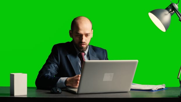 Team leader analyzing papers sitting over green screen, working with laptop and taking notes on papers. Caucasian businessman posing over isolated mockup backdrop, chroma key space.