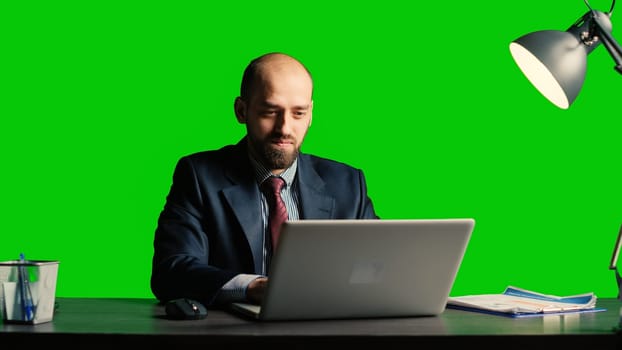 Executive manager using laptop over green screen backdrop, using computer at desk. Confident corporate employee posing on blank chroma key template, isolated copyspace background.